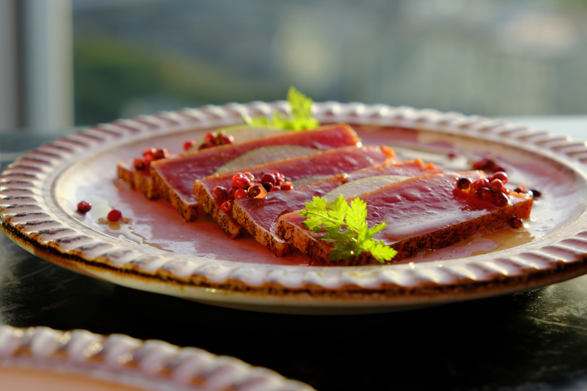 Sitzwohl Restaurant – Slices of seared tuna with pink peppercorns and herbs on a scalloped plate
